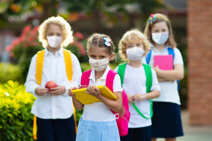School child wearing face mask during corona virus and flu outbreak. Boy and girl going back to school after covid-19 quarantine and lockdown. Group of kids in masks for coronavirus prevention.
