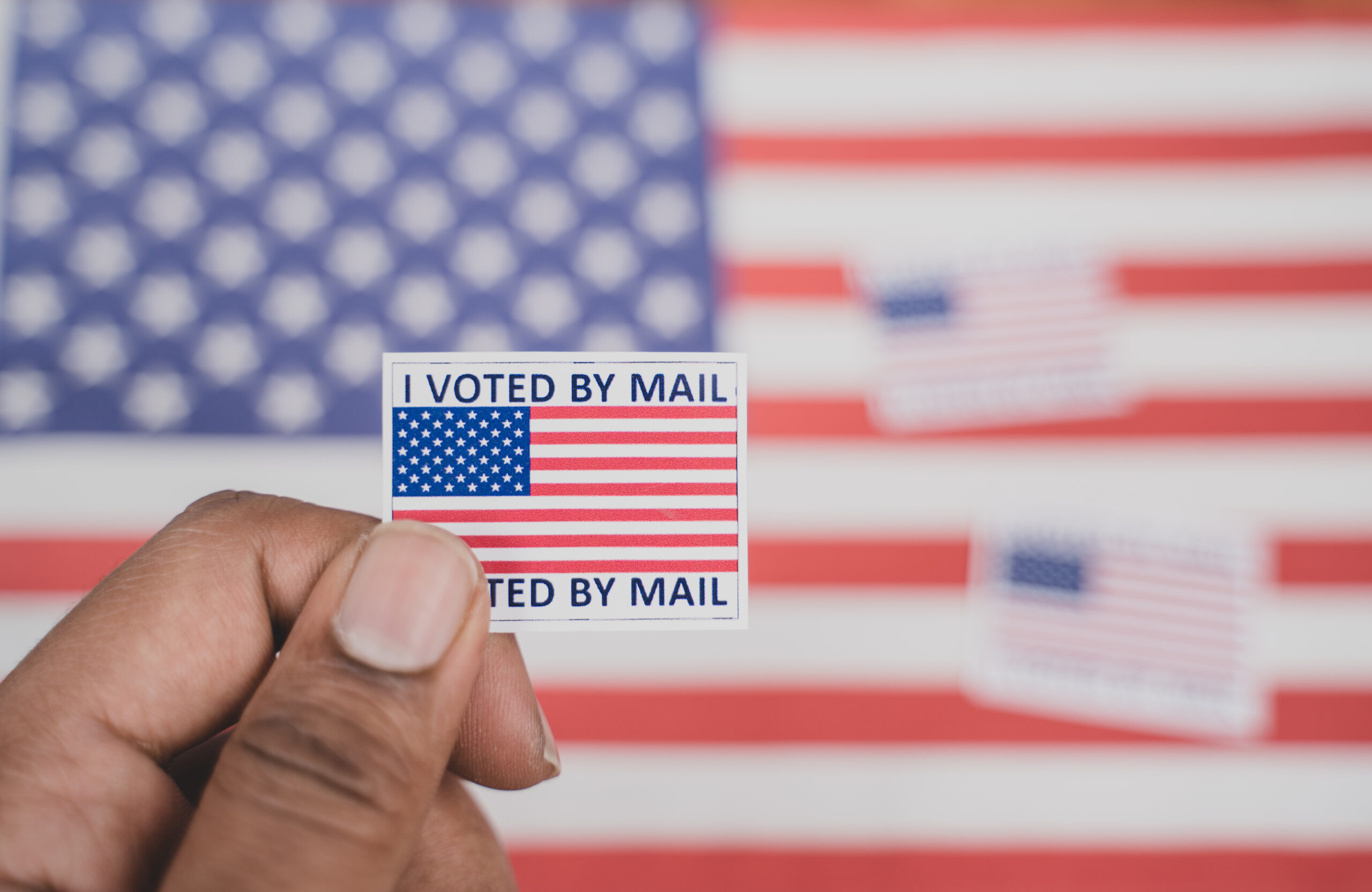 Mail-in Ballot in front of an American flag with an "I voted by mail" sticker