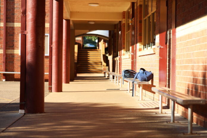 Interesting view of school buildings and outdoor yard with bricks, steps, stairs, pillars and seats. School bags on a bench seat outside classrooms. Typical high school