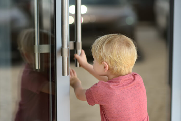 Little boy opens the glass door of the entrance. Preschool or school. Independent child