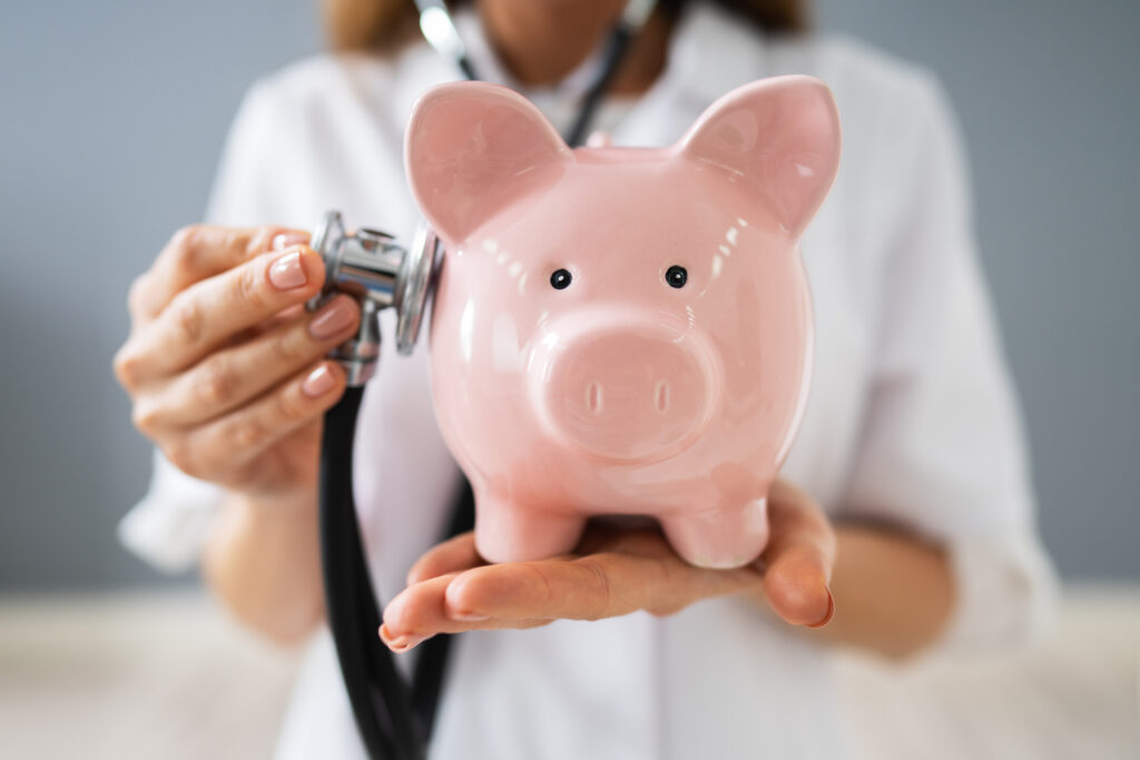 Midsection Of Young Female Doctor Holding Piggybank In Clinic