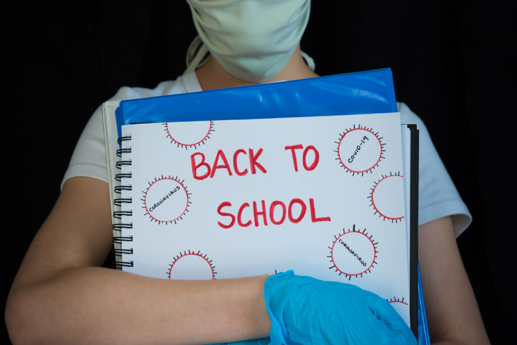 Concept photo of student returning to school during the COVID-19 pandemic. Studio shot against black background with copy space. Teenage girl holding school books and wearing protective gear.