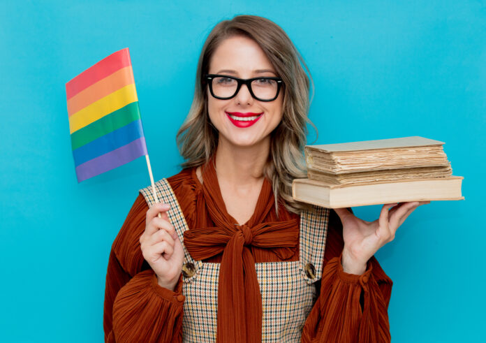 Young woman with books and LGBT flag on blue bckground