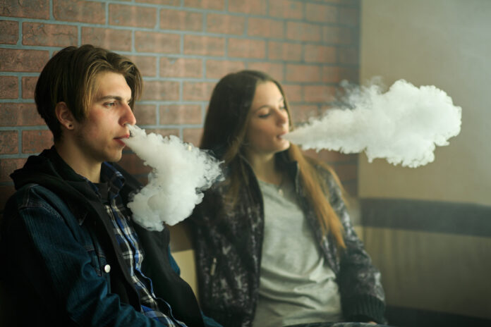 Vape teenagers. Young cute girl in sunglasses and young handsome guy smoke an electronic cigarettes in the vape bar. Bad habit that is harmful to health. Vaping activity.