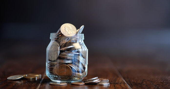 Coins in a glass jar on a wooden floor. Pocket savings from coins in the bank. Piggy bank in a glass jar with coins.