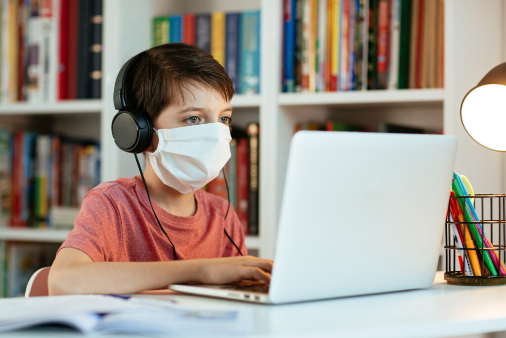 Young student wearing surgical mask doing his homework on computer.