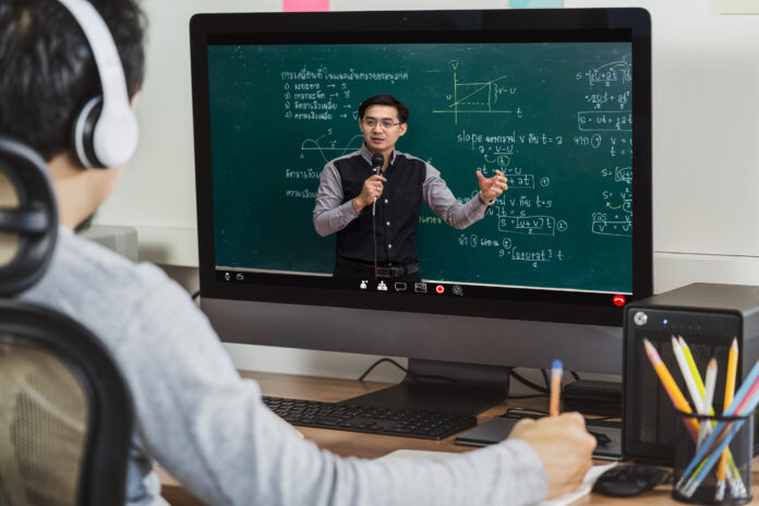 education and Social distancing concept, Rear View of Asian student learning with teacher over the physics formular in thai laguage on black board via video call conference when Covid-19 pandemic