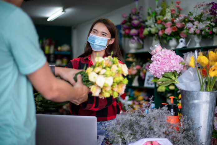 Asian Woman wearing a face mask or protective mask against coronavirus crisis, Florist owner of a small florist business holding flowers for delivery to customers at her store, small businesses