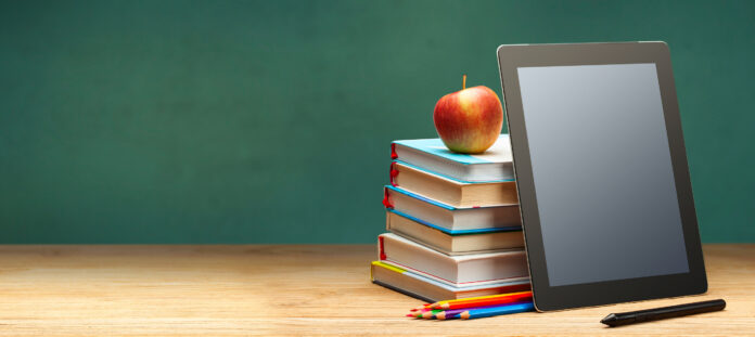 Online education. Books and tablet on the desktop on blackboard background. Copy space for text