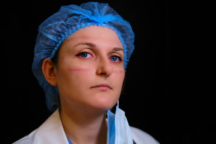 Portrait of a doctor with cuts and red eyes. Close-up of a nurse in a face mask on a black background with traces of protective clothing.