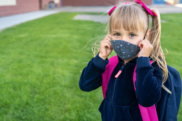 Young student caucasian girl looking at camera and wear protective face mask before school day. Ready for new school year with pandemic restrictions. School reopen. Return back to school. Copy space.
