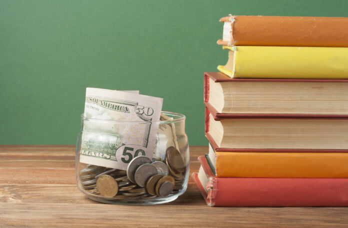 Coins in glass jar and stack of books on wooden table.Concept of funding education.