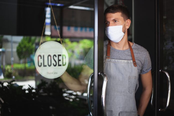 Chef in safety mask hanging up sign closed on restaurant door.