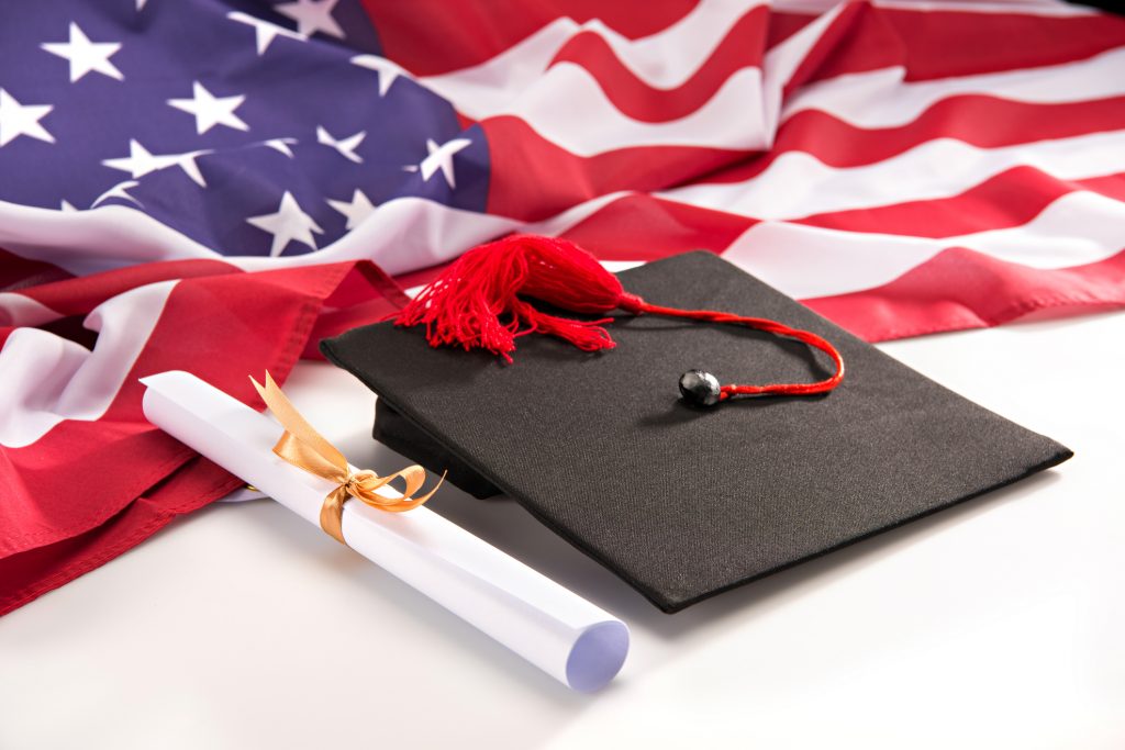 Close-up view of graduation mortarboard, diploma and us flag on white, education concept, Washington