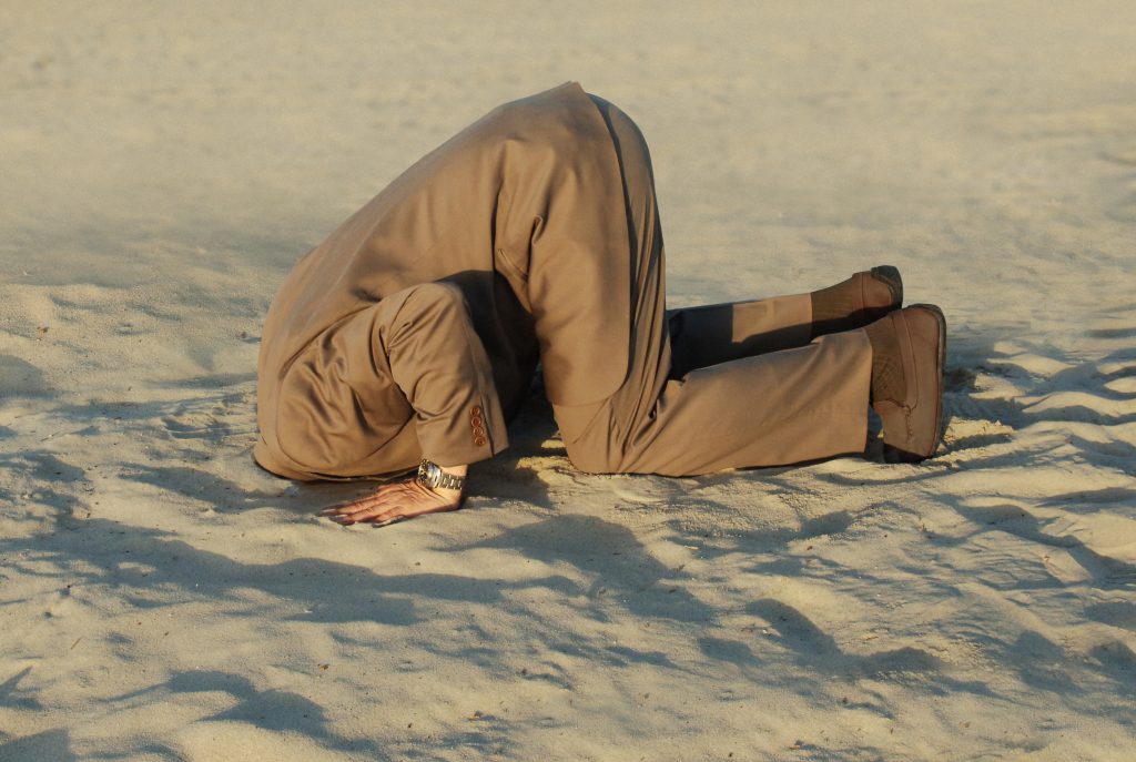 business man with his head buried in the sand, ignorance