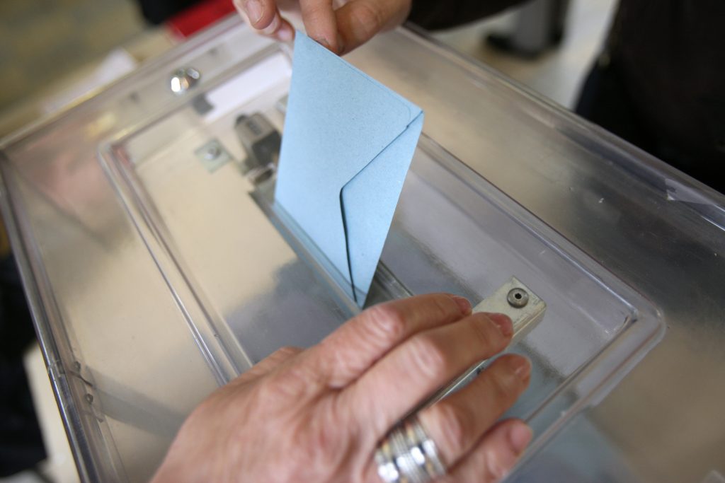 France. 05/06/2012. This colorful image depicts a man placing an election envelope in a plastic ballot box at a polling station.