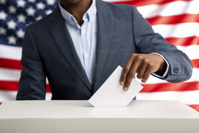Election or referendum in America. African american man holds envelope in hand above vote ballot. USA flag on background.