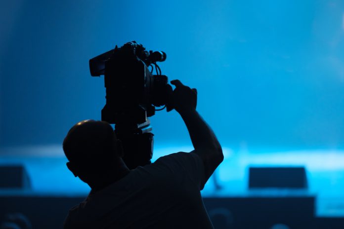 Silhouette of a cameraman with a video camera engaged in video filming in the hall.