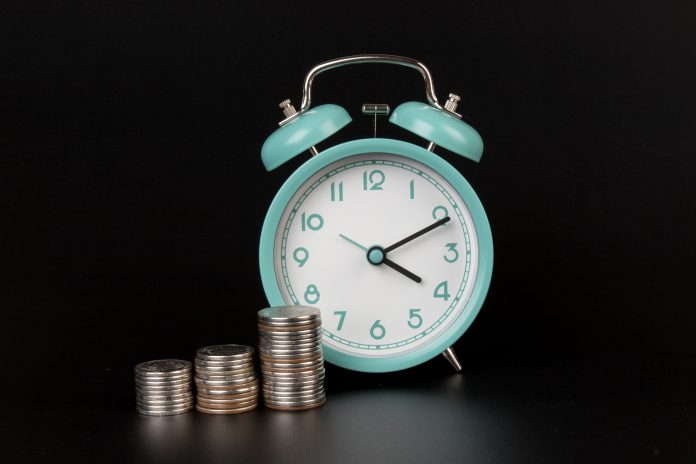 Business metaphor concept time is money concept. Blue alarm clock and coins on black background